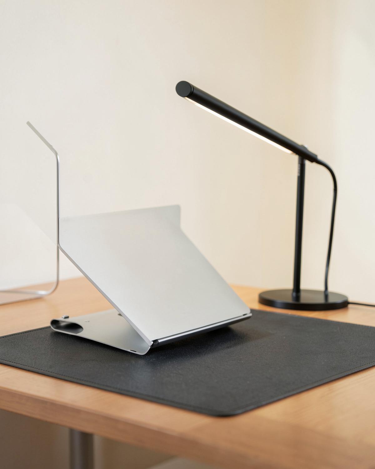 Support laptop, lampe de bureau et tapis de bureau sur un plan de travail en bois clair